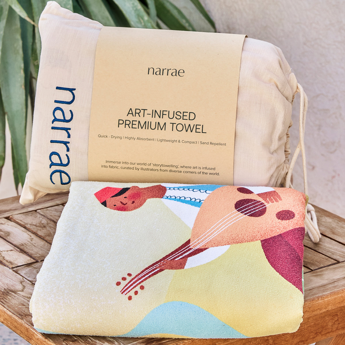 A Journey Home beach towel folded with its Narrae drawstring bag, showing an oud player in the artwork