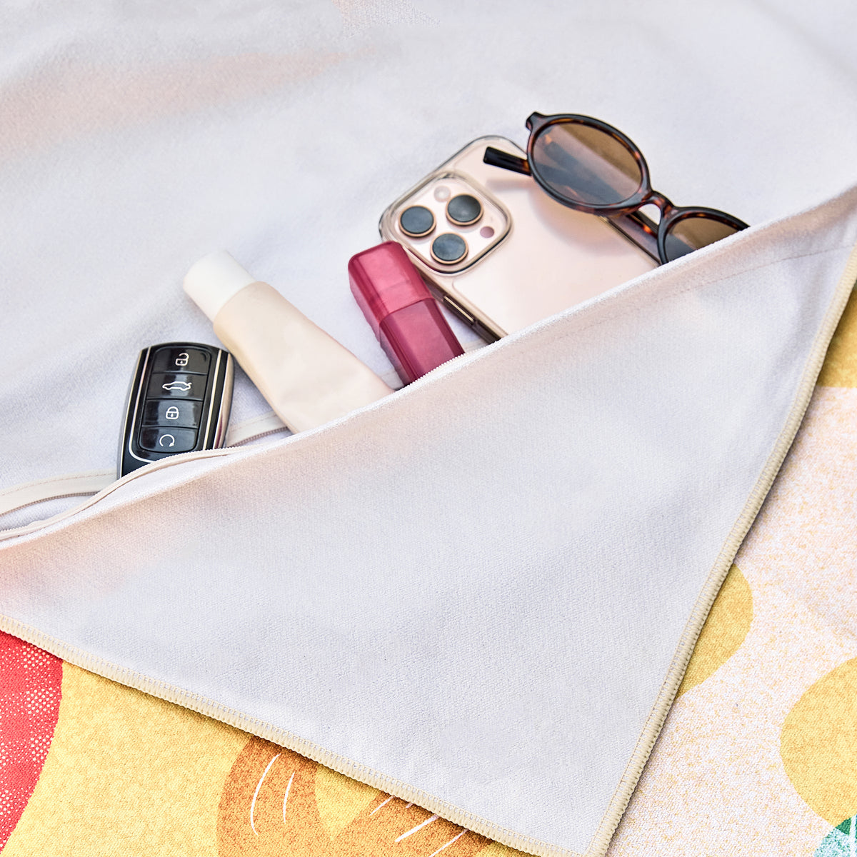 Hidden zip pocket under the A Journey Home beach towel holding a phone, sunglasses and keys