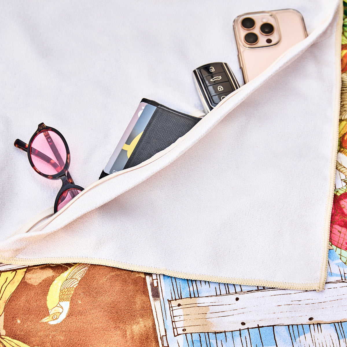 Hidden zip pocket under the Saudade beach towel holding a phone, sunglasses and a wallet